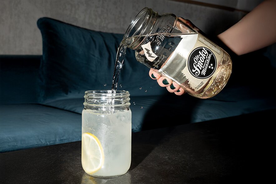 A hand pouring a jar of Ole Smoky Moonshine into a glass of lemonade.