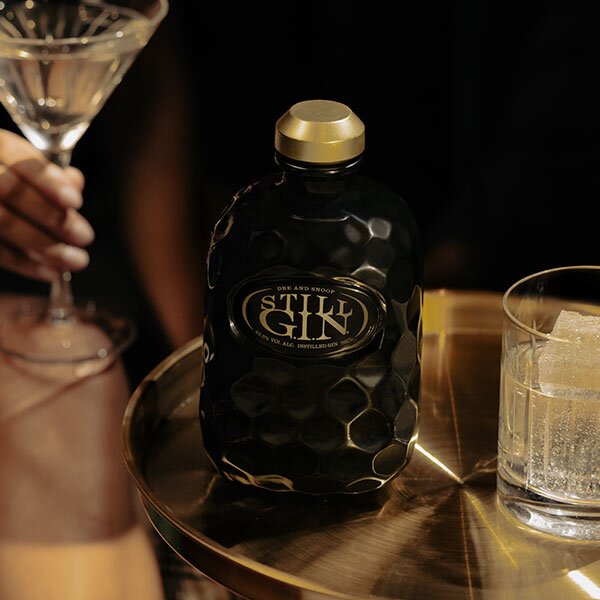 A hand holding a glass next to a bottle of Still G.I.N