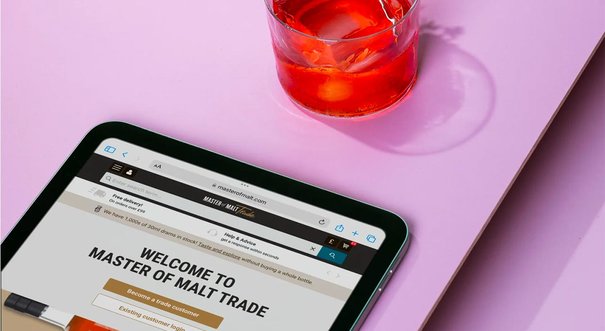 iPad with Master of Malt Trade page loaded, cocktail above on a pink table.