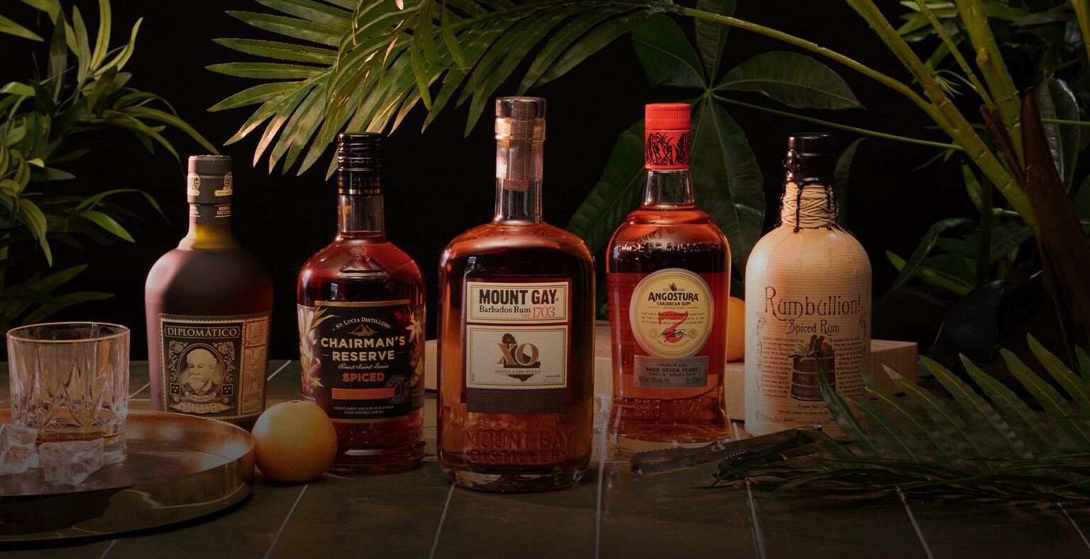 Five bottles of rum with tropical plants in the background, and a glass of rum to the left.