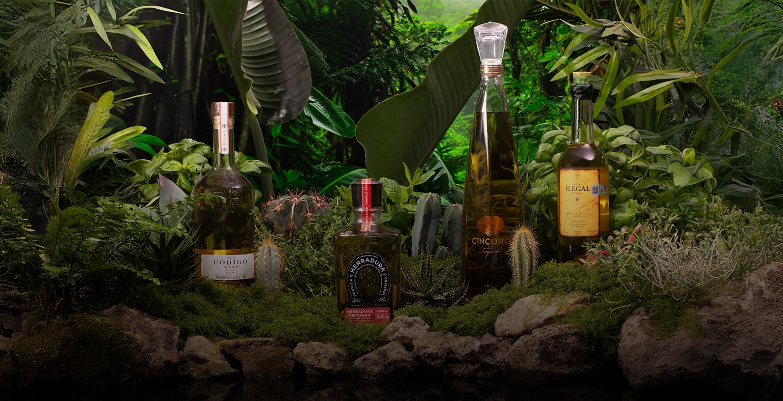Four bottles of tequila and mezcal against a rainforest background.
