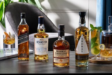Four bottles of whisky next to cocktails.