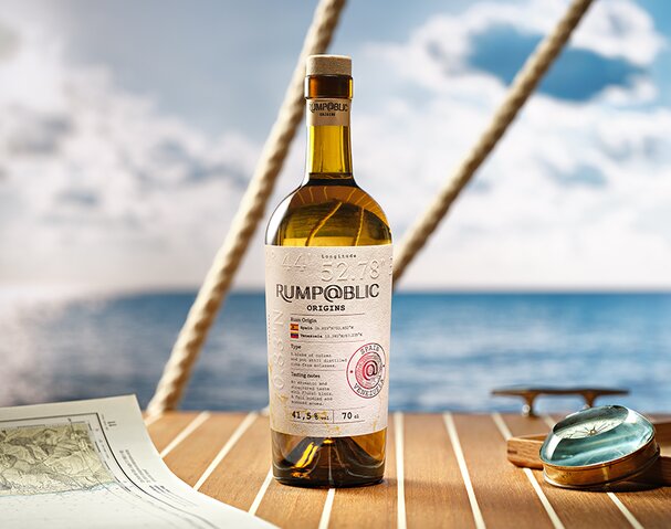 A bottle of Rump@blic Origins Spain/Venezuela on a boat deck next to a compass and map. 