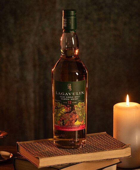 A bottle of Lagavulin 12 year old whisky on top of a stack of books next to a candle. 