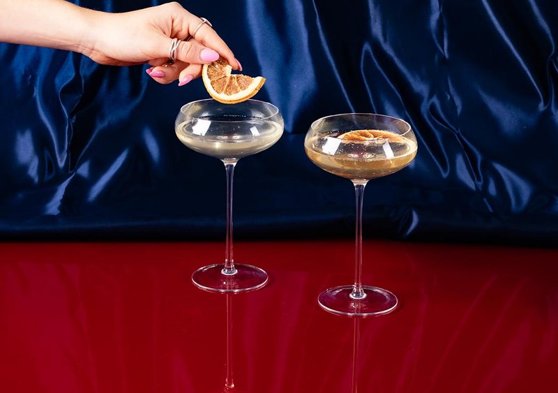 A hand placing a dried piece of fruit in a retro styled cocktail