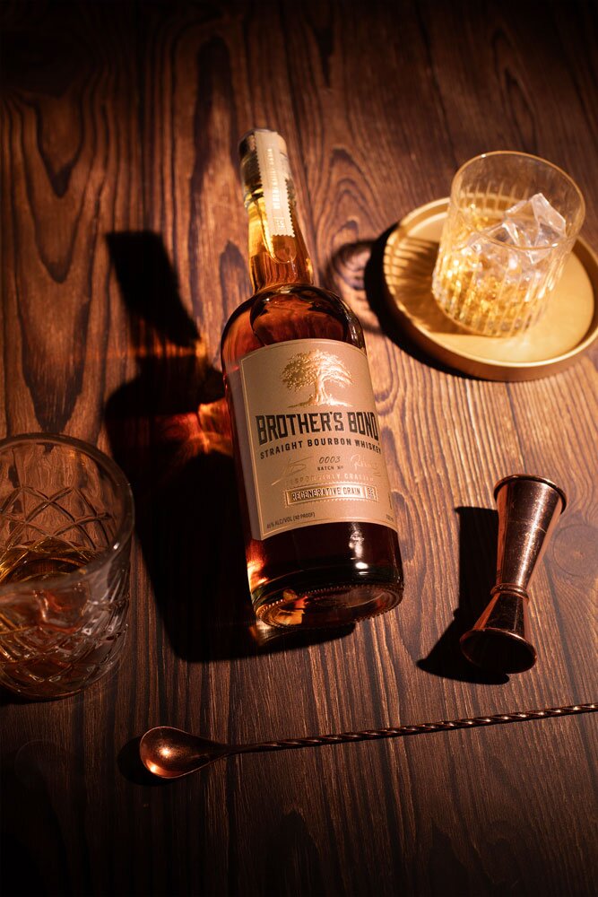 Brother's Bond Regenerative Grain bourbon whiskey bottle with glass and barware