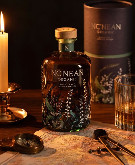 A bottle of Nc'nean organic whisky next to a candle, map of Scotland and compass.