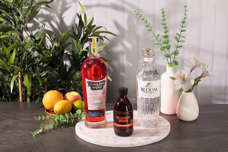 Three bottles of spirit on a white background surrounded by plants. 