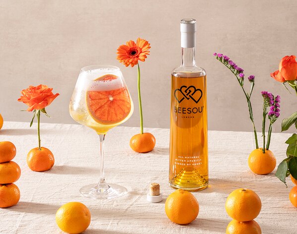 A bottle of Beesou Liqueur with a Beesou Spritz on the left of it. 