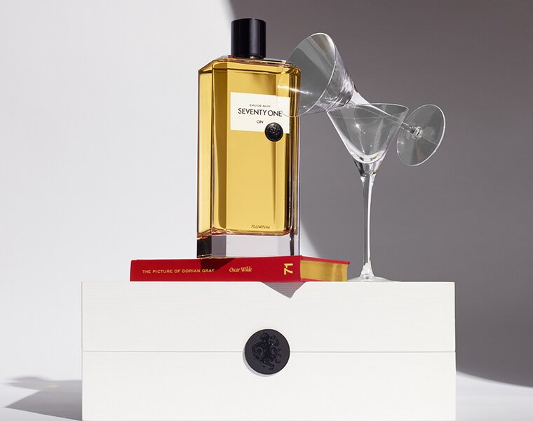 A bottle of Seventy One Gin on a white box next to two martini glasses balanced on each other. 