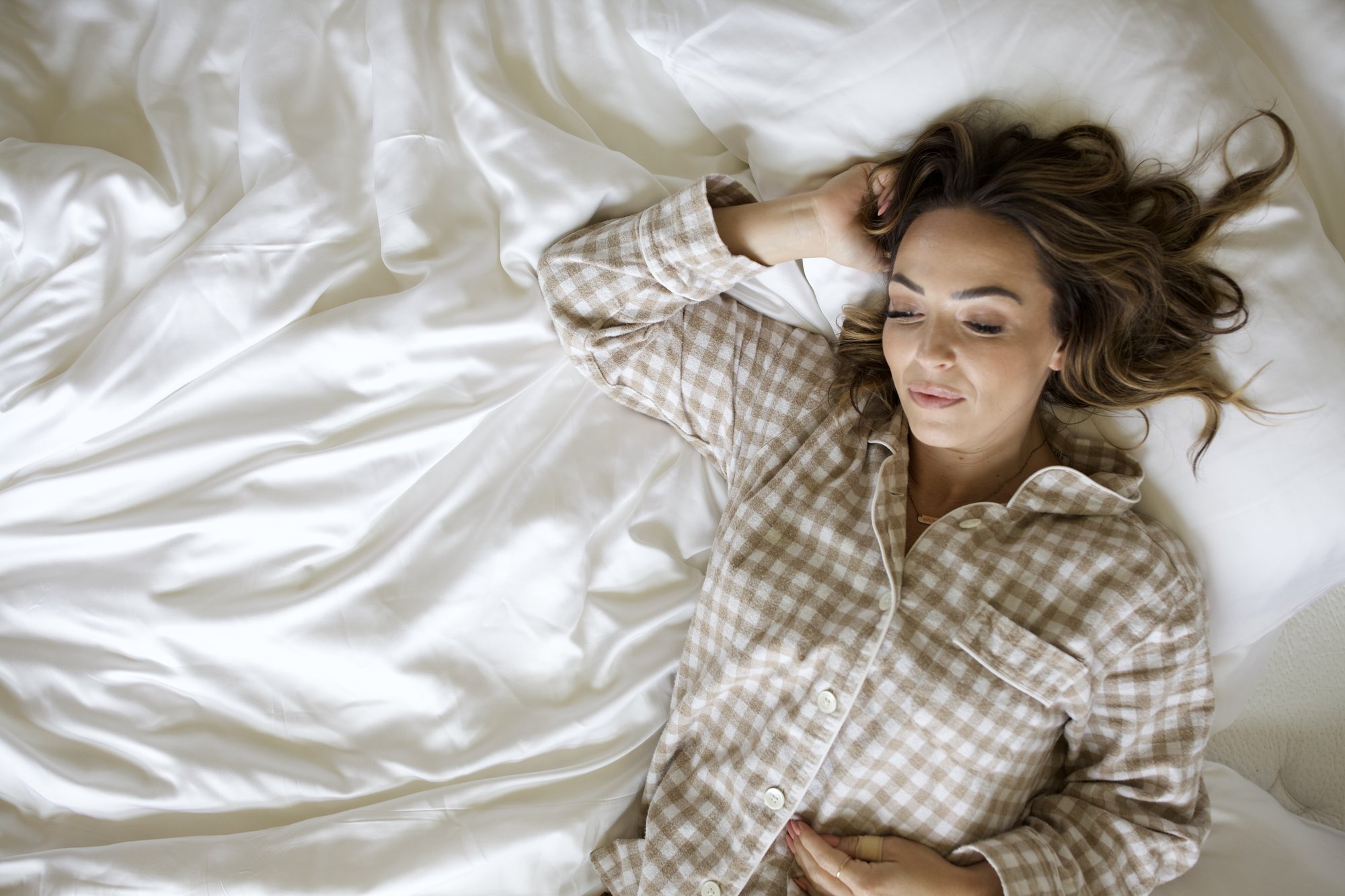 Woman in flannel pajamas lying in bed on her back