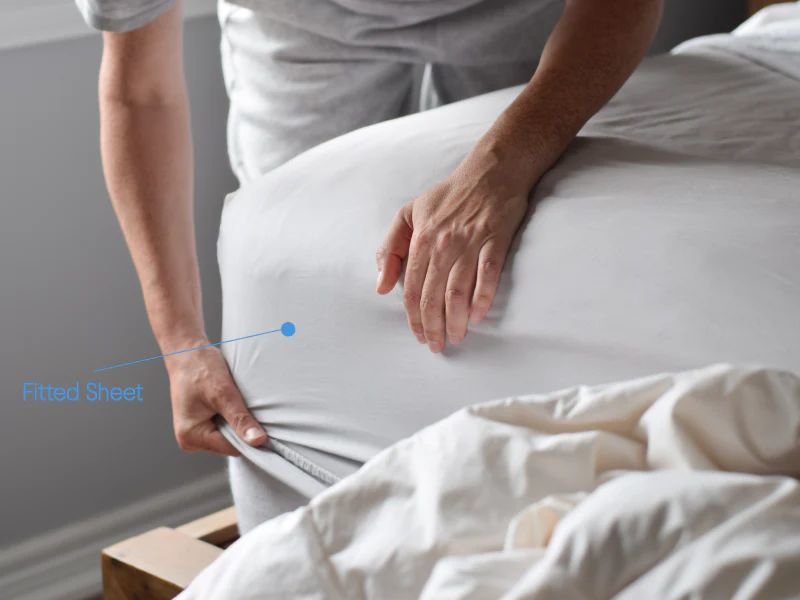 Man putting fitted sheet on bed