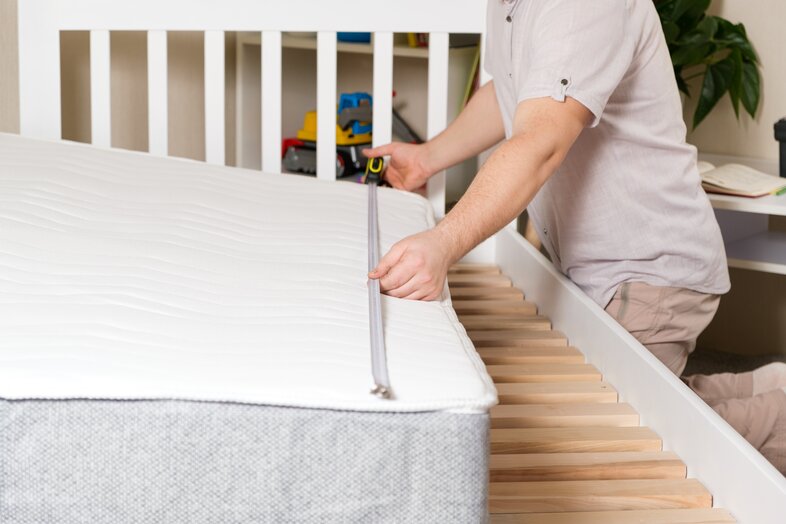 Man preparing to transport a mattress by measuring its length with a measuring tape.
