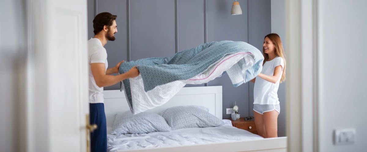 Man and woman putting bed sheet on bed