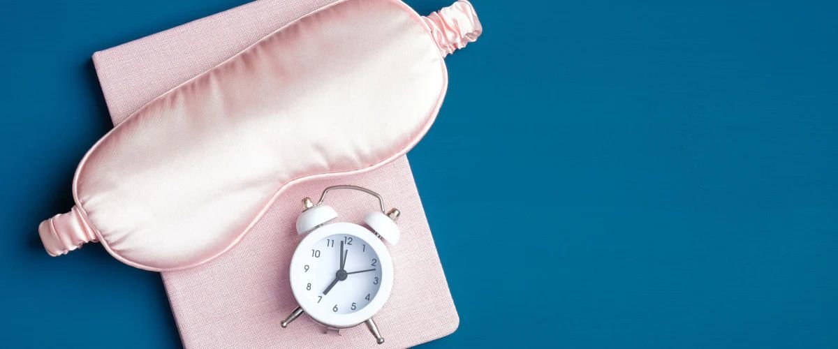 Pink sleep mask and alarm clock on top of a sleep journal
