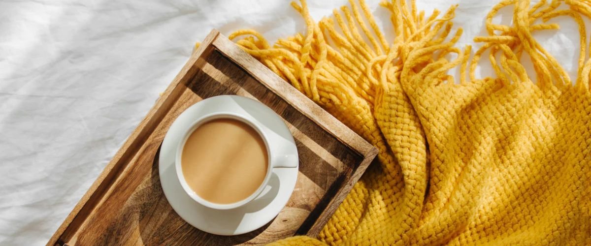 Yellow throw blanket with wood tray and cup of coffee on top