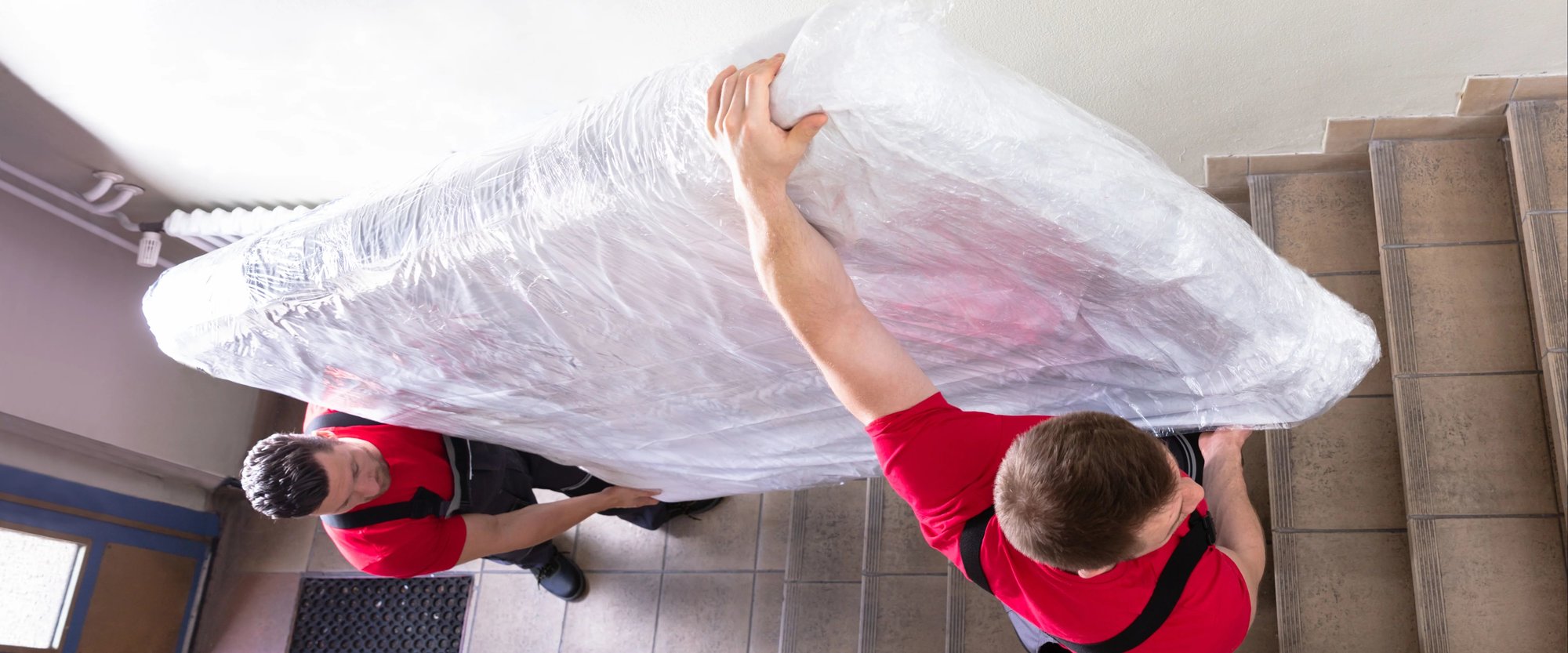 Movers carrying a mattress wrapped in plastic up the stairs