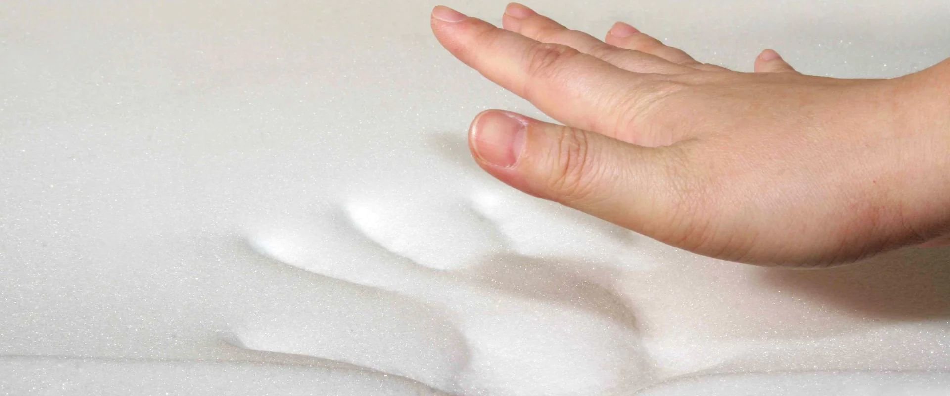 Hand pressing on a memory foam mattress, leaving an impression