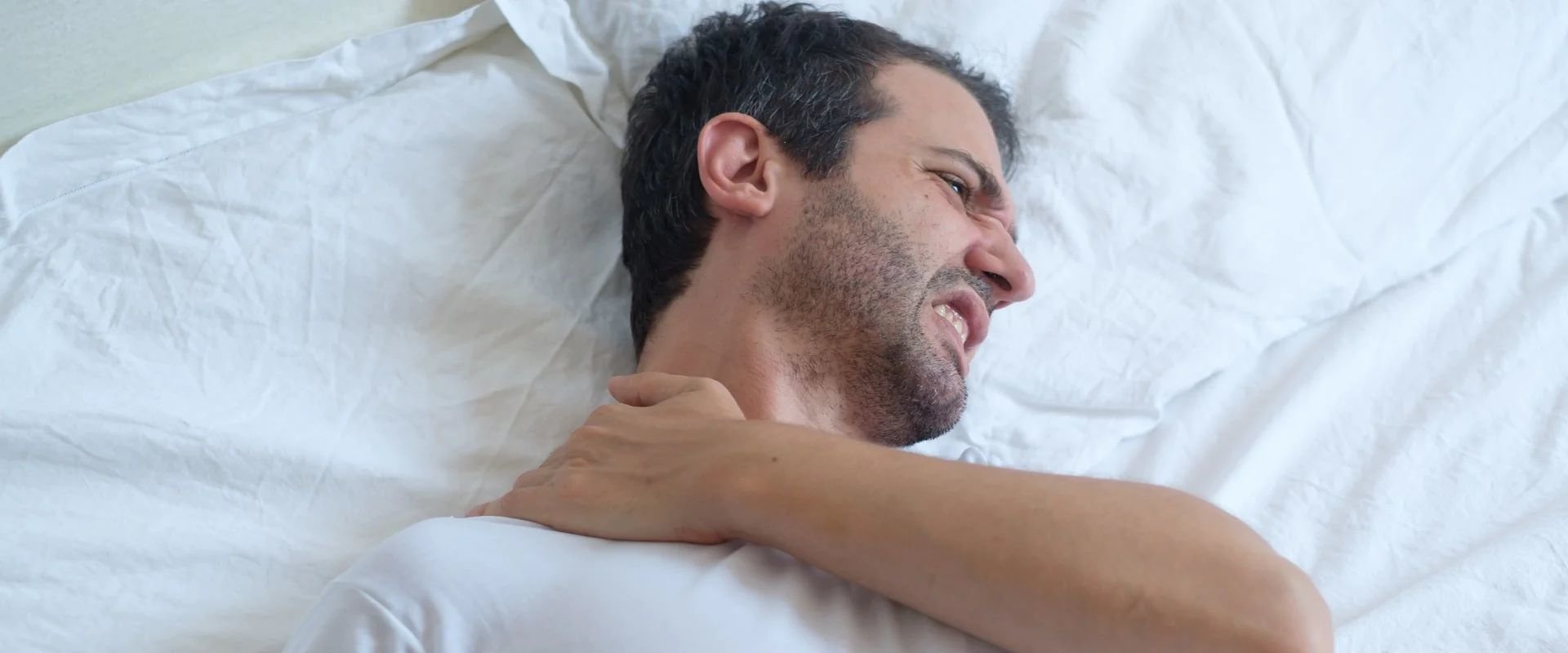 Man lying down on mattress holding his shoulder due to shoulder pain