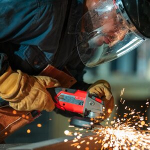 Worker wearing a faceshield and leather gloves while cutting metal with sparks flying
