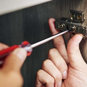 Using a screwdriver to adjust a cabinet door hinge