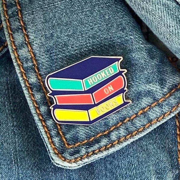 Enamel pin badge shaped like a stack of books reading Hooked on Books