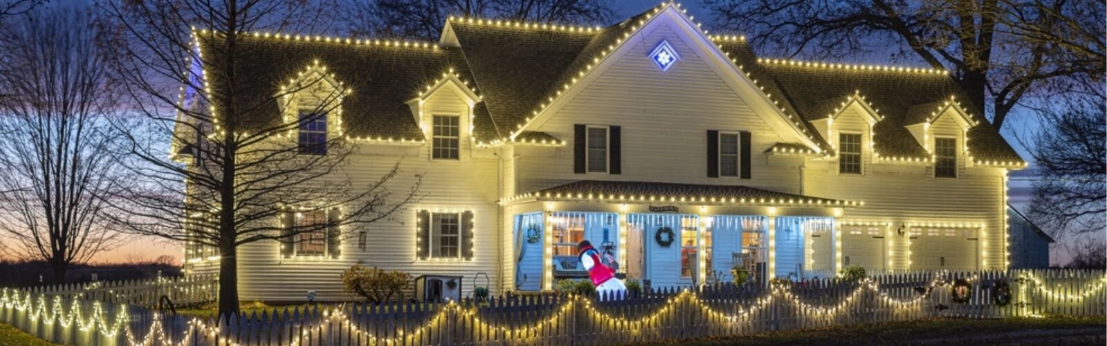 Mother and daughter snuggling in front of a Christmas tree wearing Santa hats while holding Christmas lights