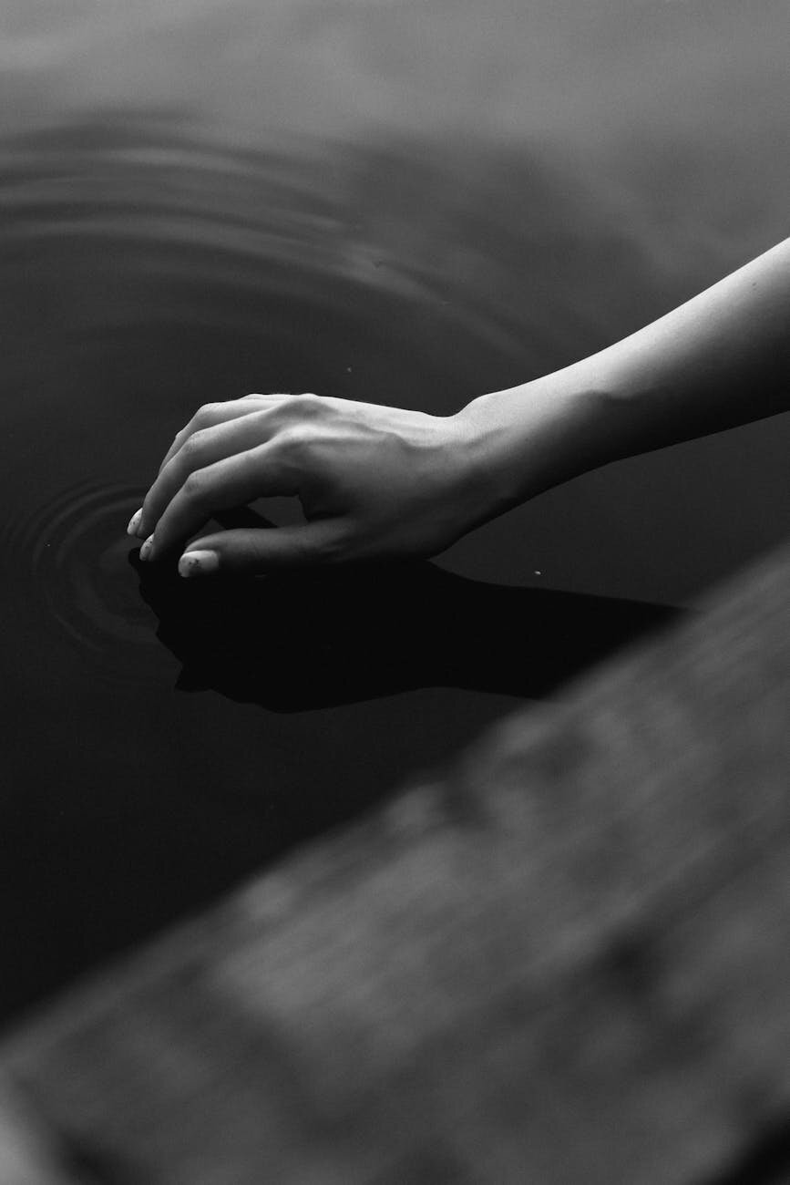 An image of a hand touching still water and creating a gentle ripple effect