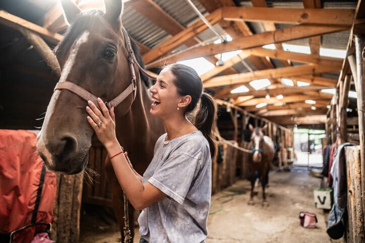Laughing woman walking with horse inside a stable. 