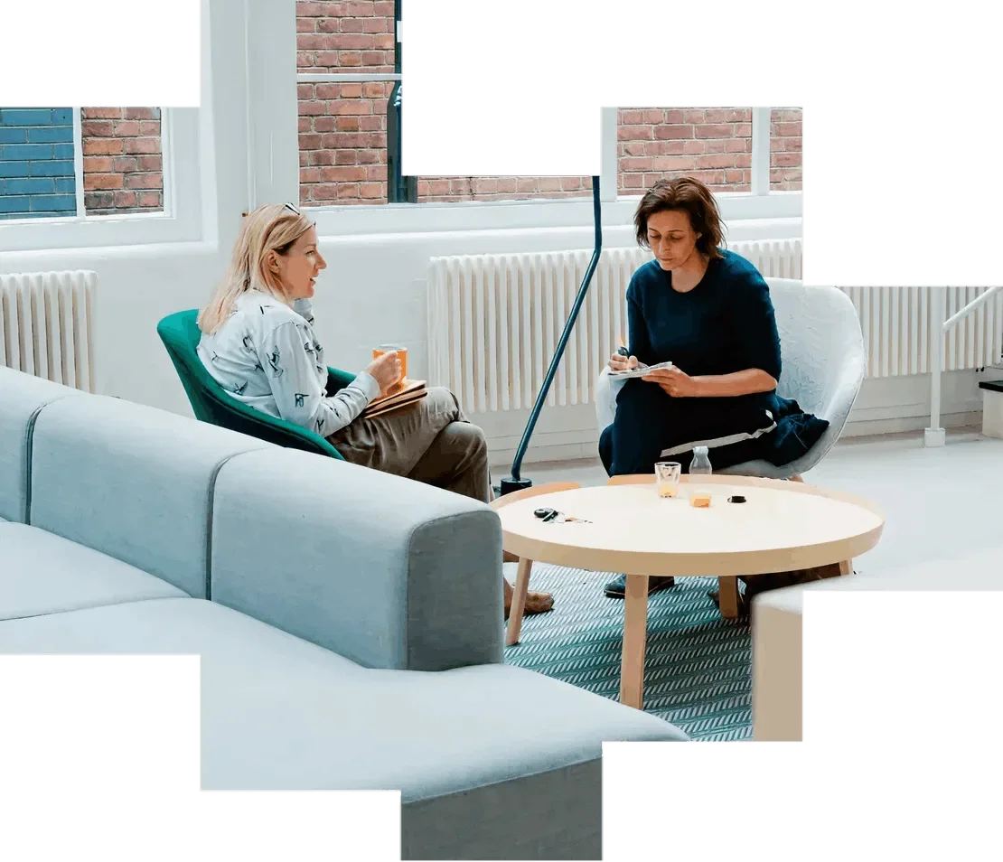 Two women in an office sitting on chairs, talking