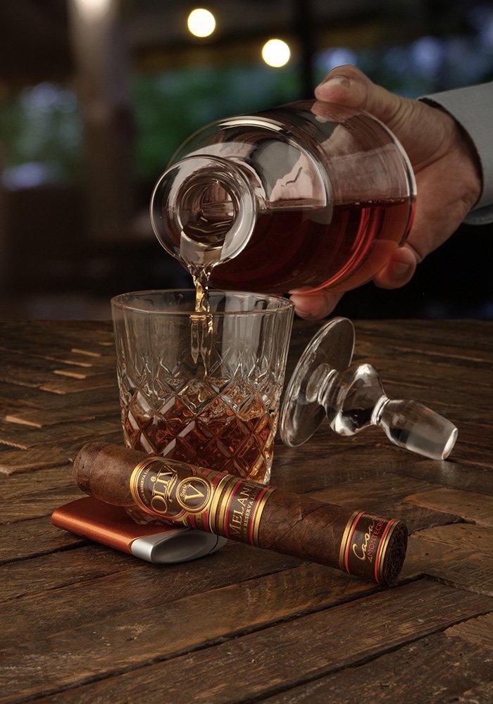 an image of the OLIVA SERIE V MELANIO ROUND DOUBLE ROBUSTO CDM EXCLUSIVE cigar and a drink