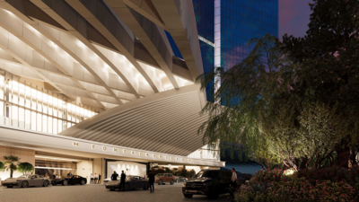 A modern building with a glass facade and geometric design, surrounded by trees. Several cars are parked in front, and people are seen walking near the entrance.