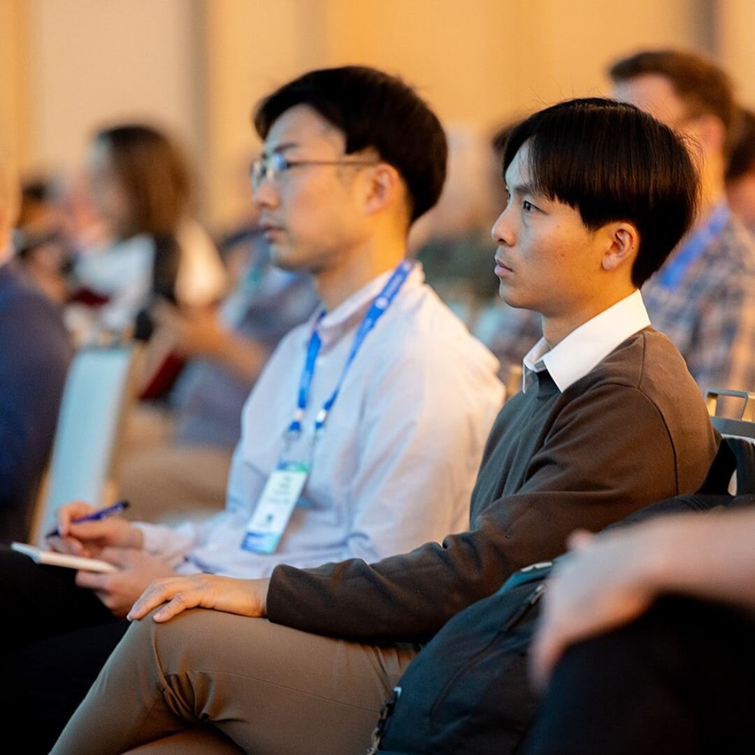 Two HumanX 2025 sitting in the audience are in focus. They are listening to a session and one of the attendees is taking notes.