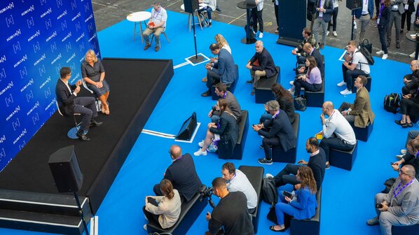 A captivated audience gathered in chairs, intently watching a mini presentation at a tech conference.