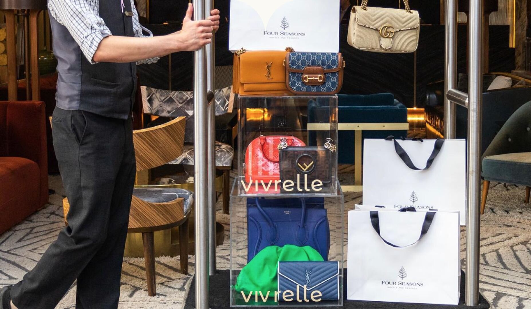 A man maneuvers a cart adorned with Vivrelle bags alongside shopping bags bearing the Four Seasons hotel emblem