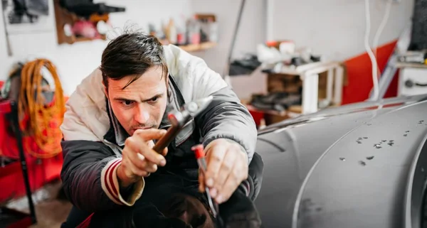 Técnico que usa luvas de proteção está em processo de reparo de amassado sem tinta no carro