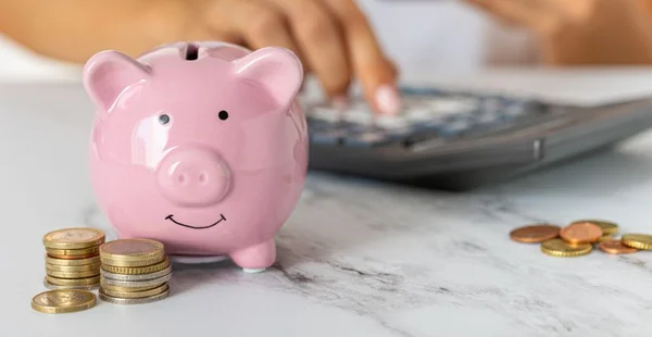 Close-up das mãos de uma mulher contando despesas em uma calculadora com um cofrinho em uma mesa de escritório. economia, crise e inflação. Gestão de Custos