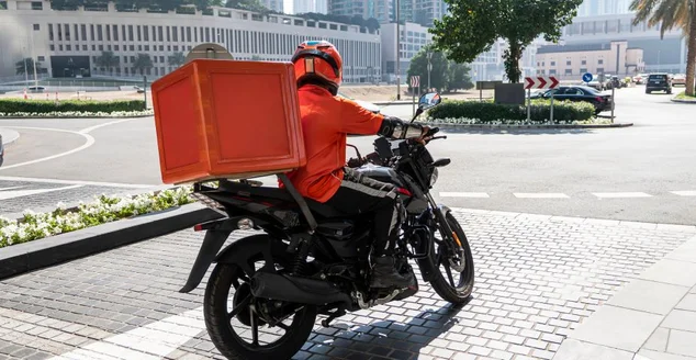 Um mensageiro de entrega de comida está dirigindo um pedido para a casa de um cliente em um ciclomotor. comida para viagem durante a quarentena. transporte de entrega de encomendas em casa. motociclista com uma mochila grande