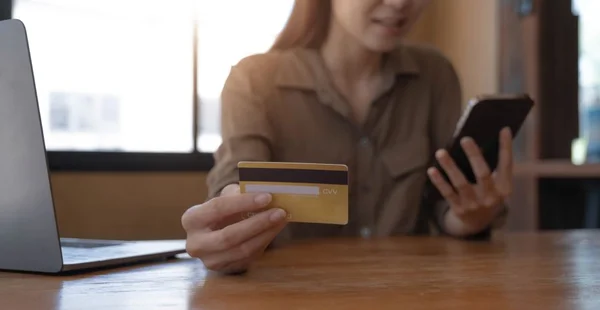 Closeup imagem da mão de uma mulher segurando o cartão de crédito e pressionando no celular na mesa de madeira no escritório