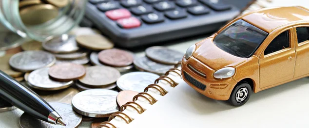 Modelo do carro em miniatura, calculadora, moedas espalhadas em frasco de vidro, papel de caderno e caneta na mesa de mesa de escritório