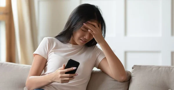 Mulher asiática chateada chorando, segurando telefone, recebeu má mensagem