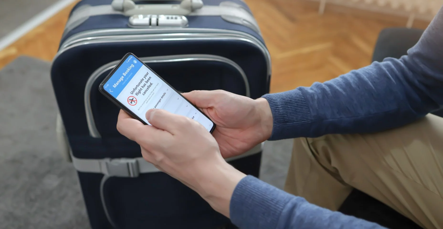 Homem segurando um smartphone com voo cancelado na tela. Notificação de voo atrasado na tela do smartphone. Homem esperando no quarto com bagagem. Agendar aplicativo, cancelar voo, reserva e conceito de seguro.