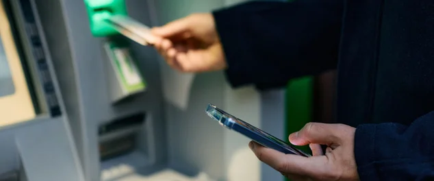 foto de acima do homem usando telefone inteligente enquanto saca dinheiro no caixa eletrônico.