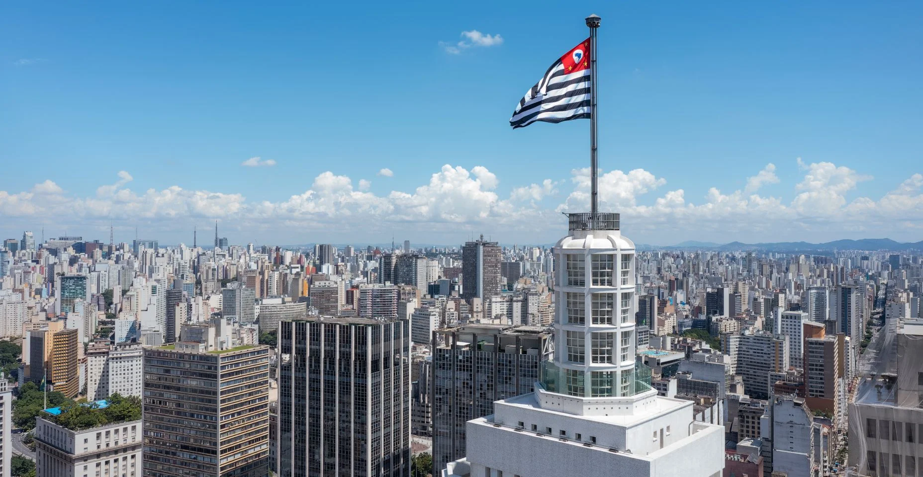Bandeira do estado de São Paulo vibrando no topo do farol santander, cidade ao fundo, céu azul