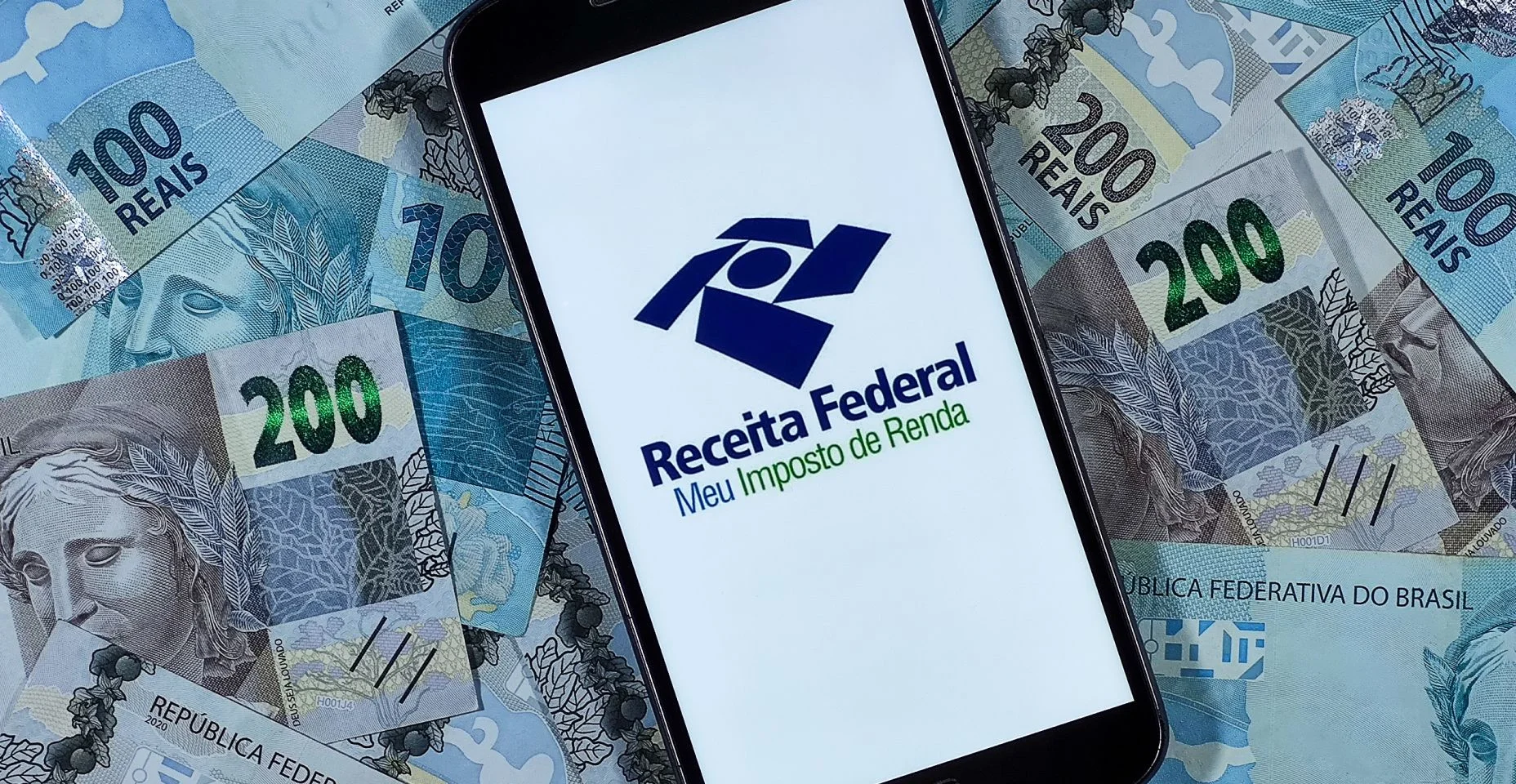 Logotipo da Receita Federal - Meu imposto de Renda na tela do smartphone com notas de 100 reais e 200 reais.