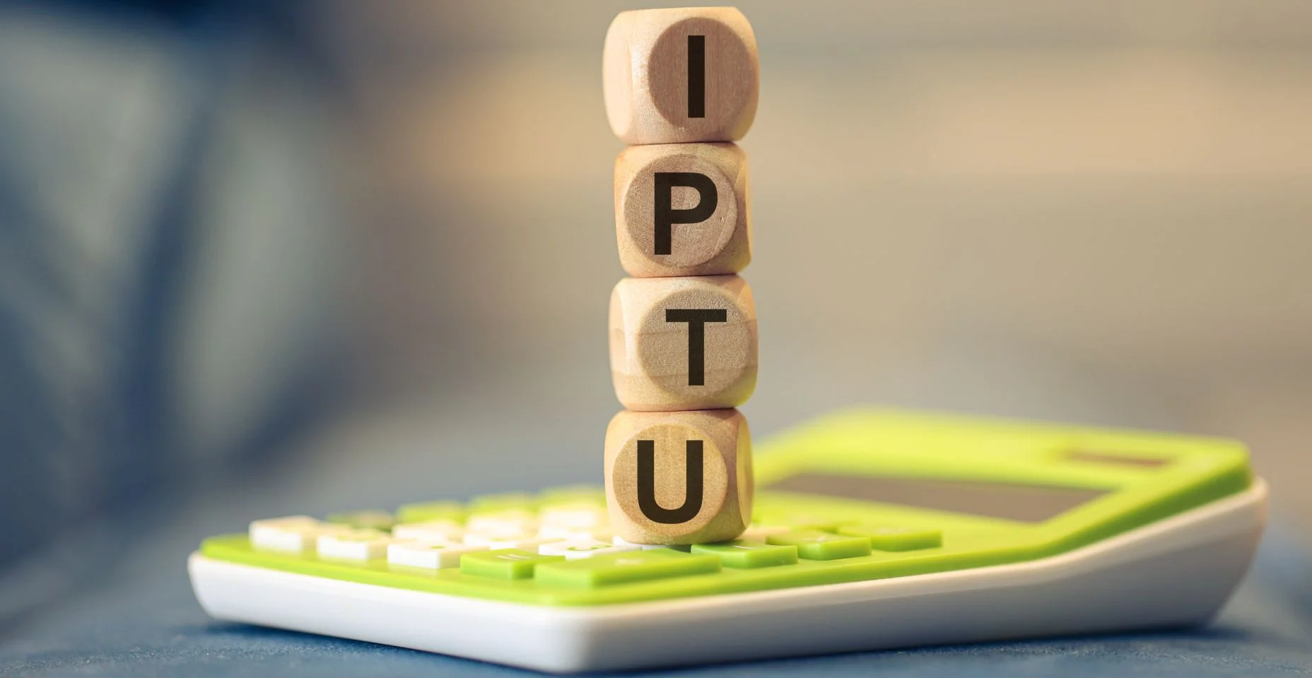 A sigla IPTU escrita em dados de madeira que estão empilhados sobre uma calculadora. Imposto sobre a Propriedade Predial e Territorial Urbana. Imposto, Brasil.