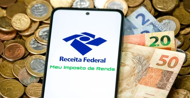Imposto de renda 2023 da receita federal com celular e moedas de reais.