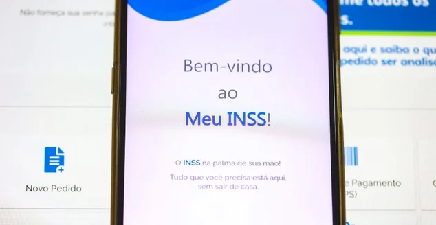 O aplicativo do INSS - Instituto Nacional do Seguro Social na tela de um telefone celular que está sobre um laptop. Aposentadoria, Benefícios, Brasil.