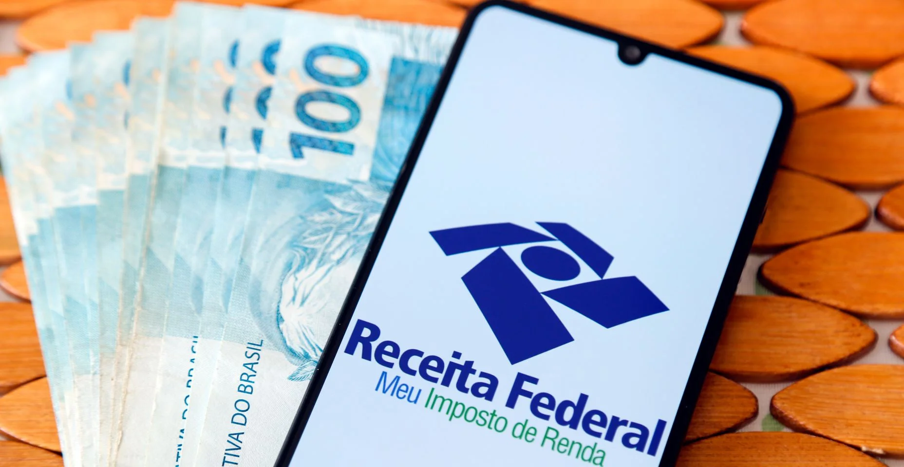 Logotipo da Receita Federal na tela do celular e notas de dinheiro brasileiro