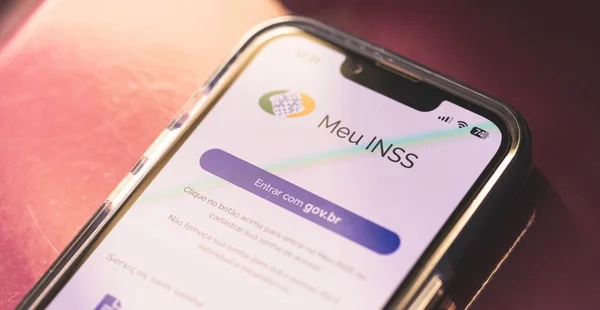 O aplicativo: Meu INSS, na tela de um smartphone sobre um móvel de madeira. Instituto Nacional do Seguro Social.